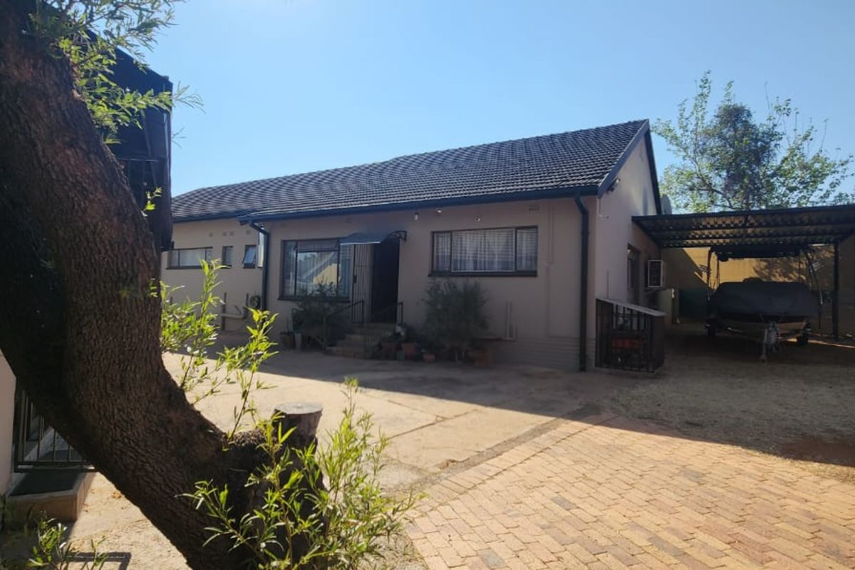 Rear view of the property featuring a paved courtyard, covered carport area, and established garden surroundings.