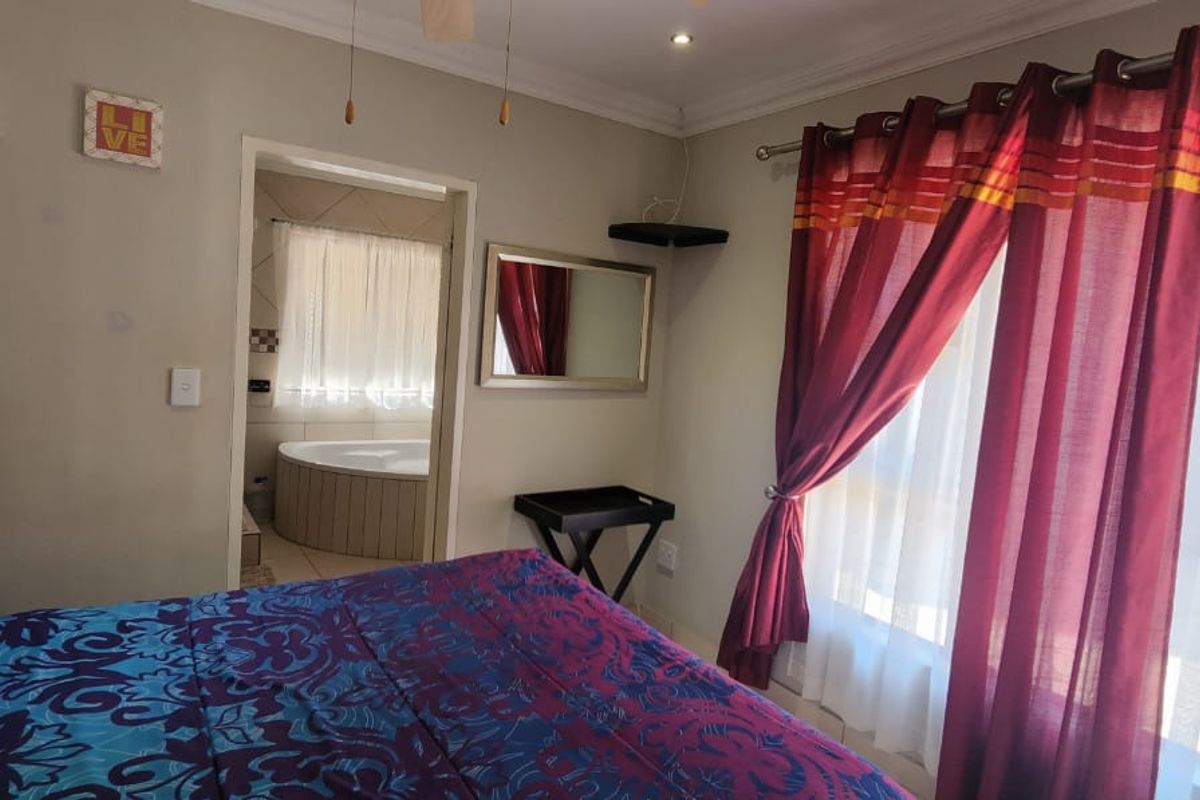 A bedroom featuring neutral walls, large windows with curtains, and an adjoining bathroom with a corner bathtub.