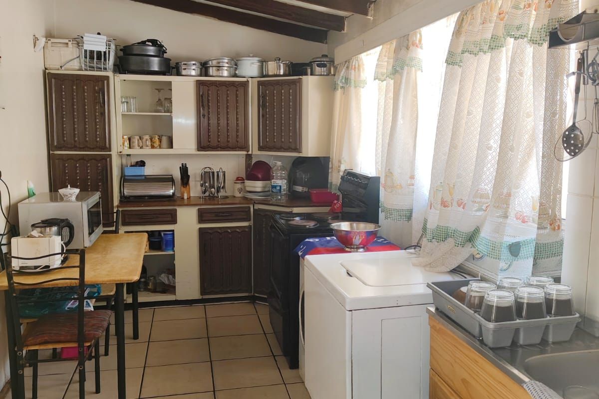 A dated kitchen featuring wooden cabinetry, exposed ceiling beams, and tiled flooring, offering a functional layout with ample storage space.