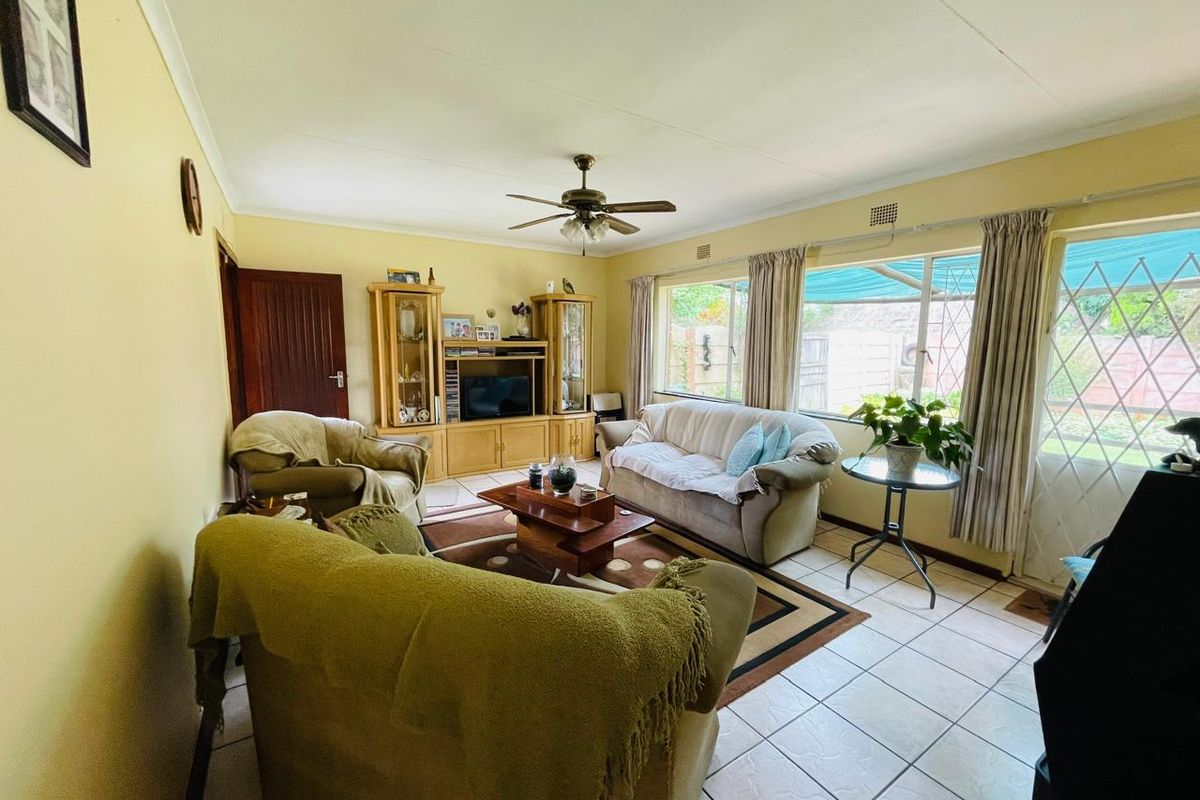 A living room featuring tiled flooring, a ceiling fan, and large windows providing natural light and access to the outdoor area.