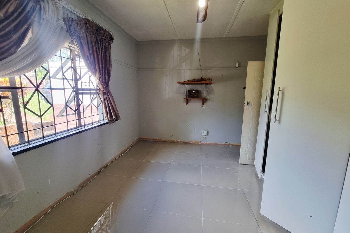 A bedroom featuring tiled flooring, built-in cupboards, and security bars on the window. The room is currently vacant and requires minor finishing touches.