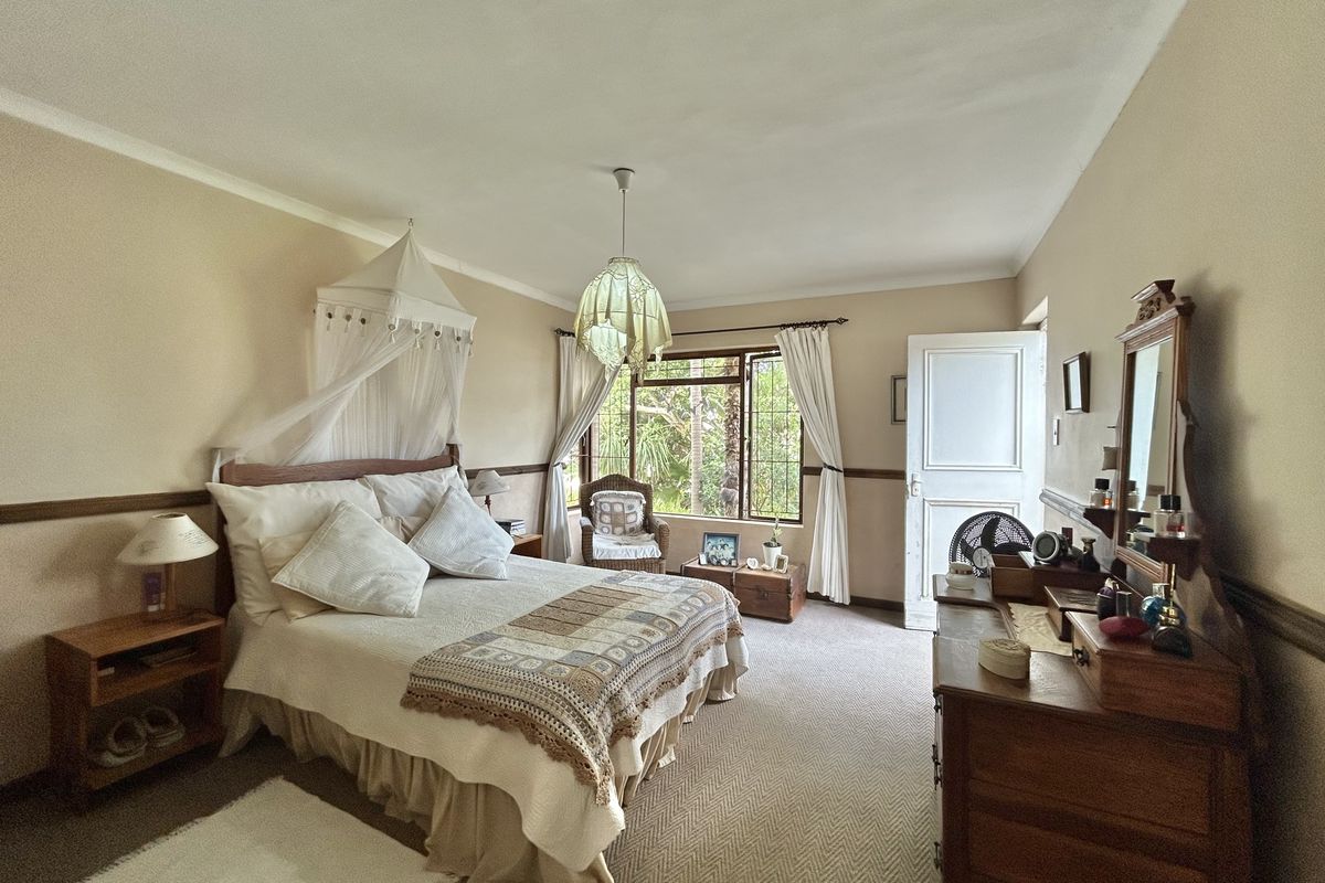 A spacious bedroom featuring neutral walls, carpeted flooring, and large windows that provide natural light and garden views.