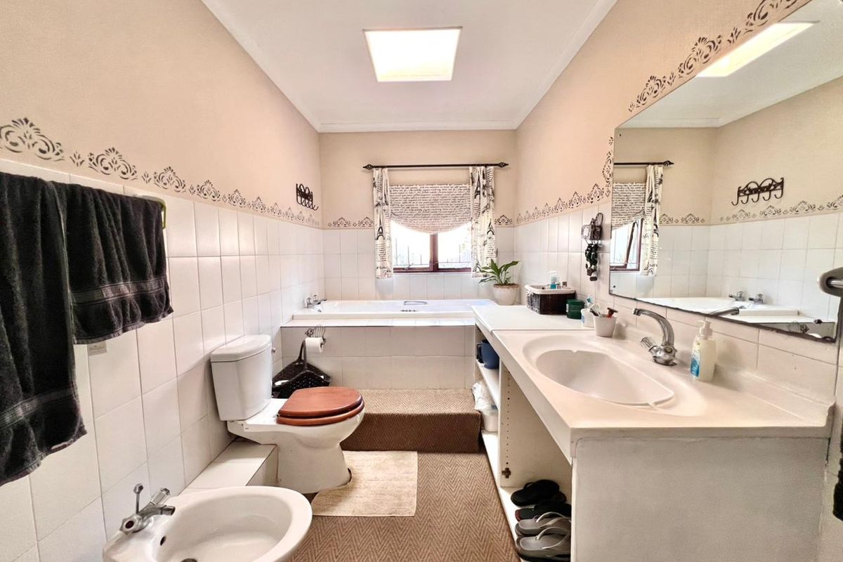 A functional bathroom featuring a built-in bathtub, a vanity with a single basin, a toilet, and a bidet, finished with half-height wall tiling.