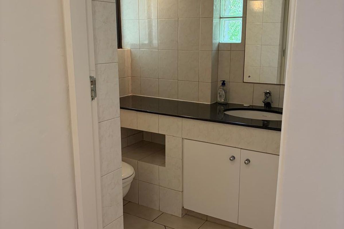 A functional bathroom featuring a vanity with a granite countertop, integrated sink, wall-mounted lighting, and glass block window detail.