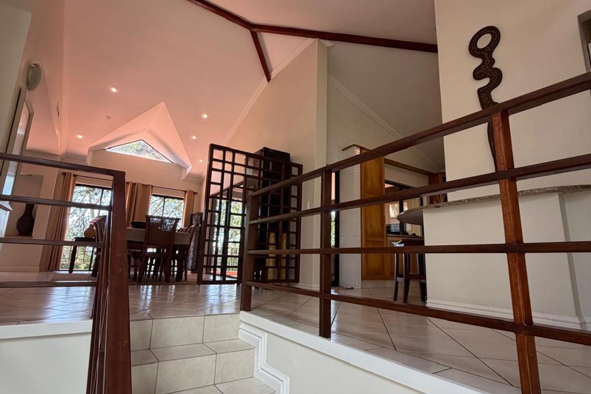 Spacious split-level living area featuring vaulted ceilings with exposed timber beams, tiled flooring, and a classic timber balustrade overlooking the lower level.