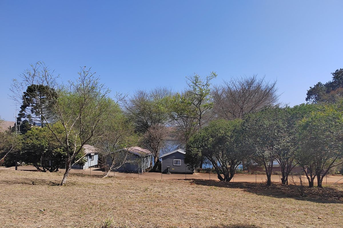 A view of the residential land featuring mature trees and small existing structures, offering potential for development or landscaping.