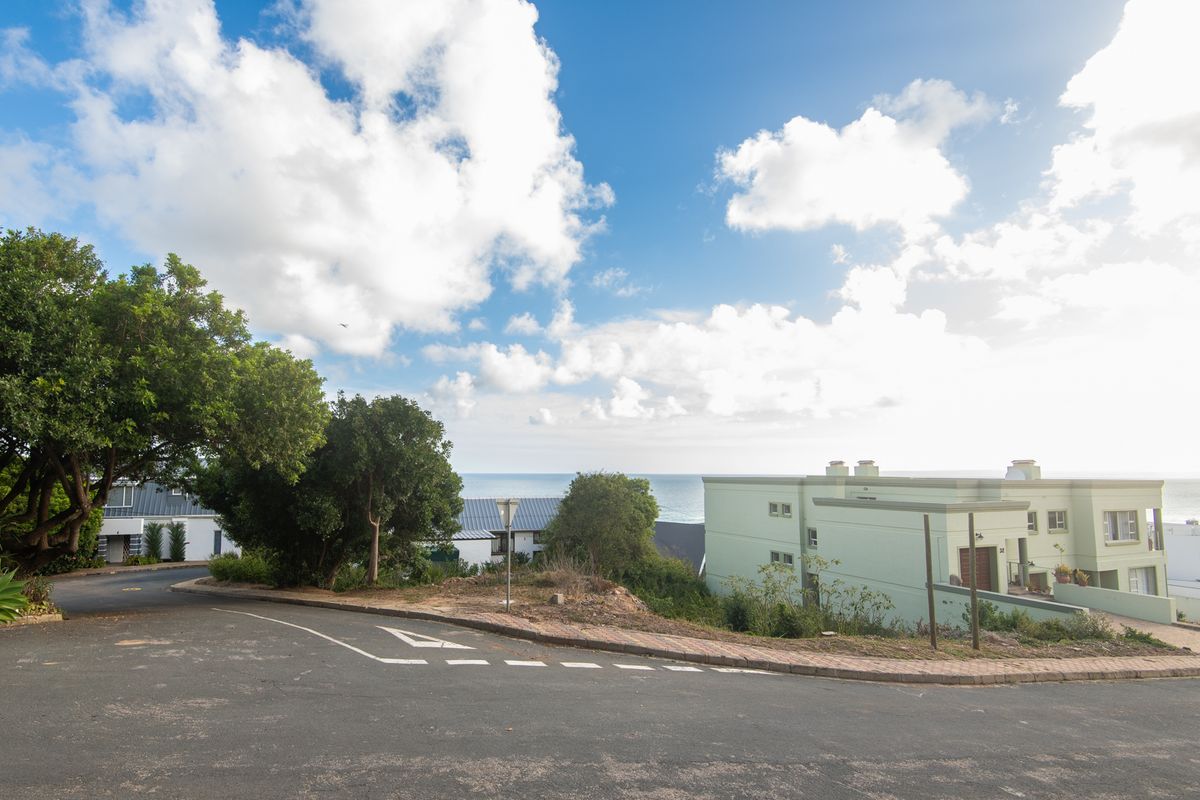 A street view of a residential area featuring paved roads, curbs, and surrounding coastal landscape with nearby residential buildings.