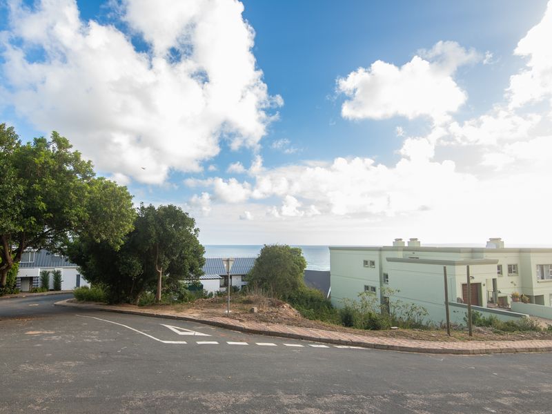 A street view of a residential area featuring paved roads, curbs, and surrounding coastal landscape with nearby residential buildings.