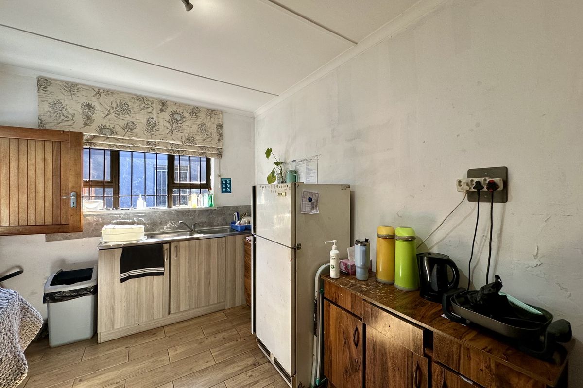 A functional kitchen area featuring wood-look cabinetry, a stainless steel sink, and tiled flooring, requiring cosmetic updates to the wall finishes.
