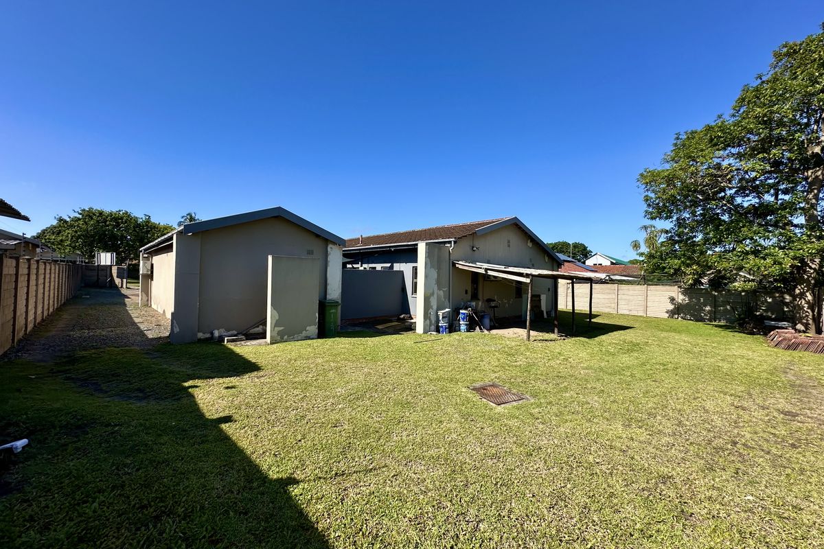 A view of the rear exterior of the house, featuring a large lawn, a detached structure, and a basic covered patio area.