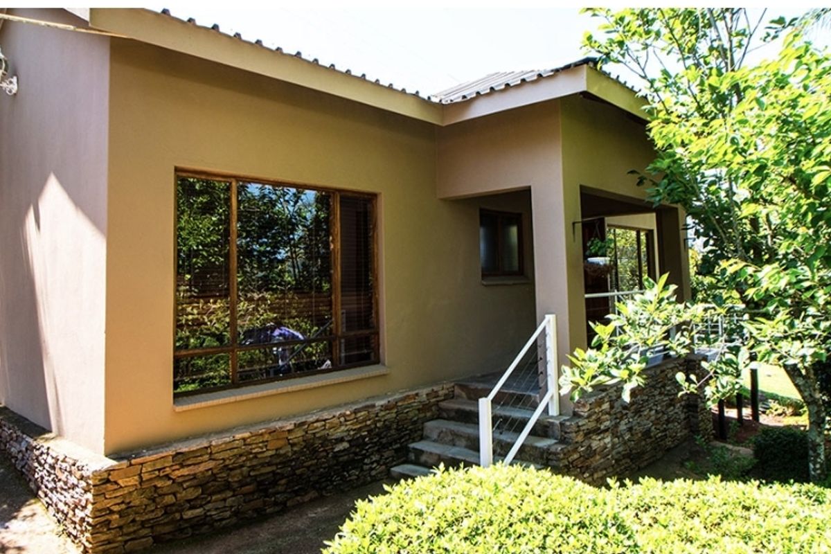 A view of the exterior rear facade featuring stone cladding, large windows, and a small staircase leading to a covered patio area.