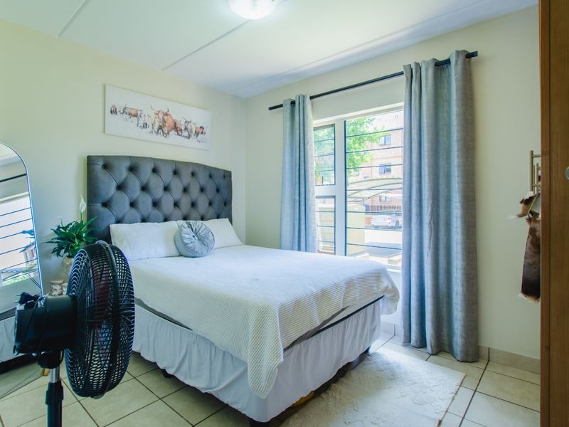 A well-lit bedroom featuring tiled flooring and a window fitted with security bars, providing a functional and comfortable living space.