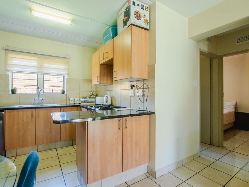 A functional kitchen featuring laminate cabinetry, granite countertops, tiled backsplash, and ceramic tile flooring, with an adjacent view into a bedroom.