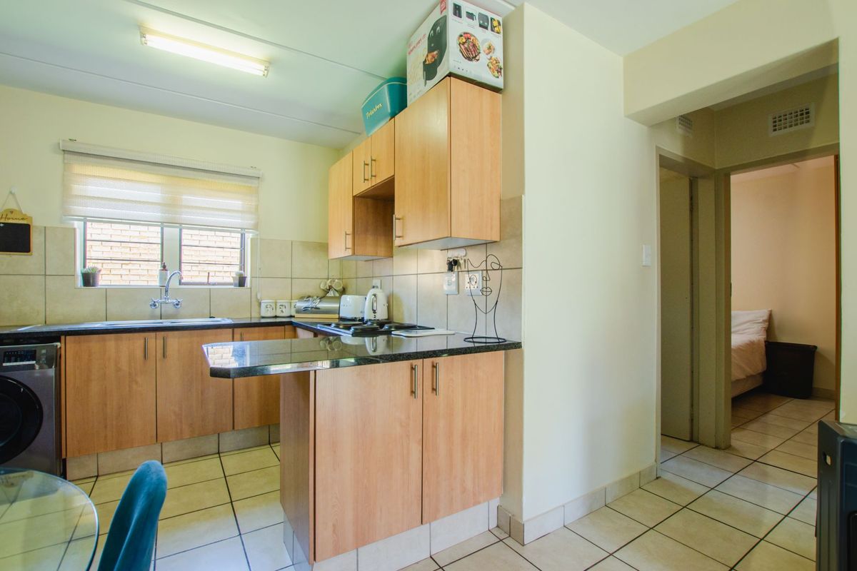 A functional kitchen featuring laminate cabinetry, granite countertops, tiled backsplash, and ceramic tile flooring, with an adjacent view into a bedroom.