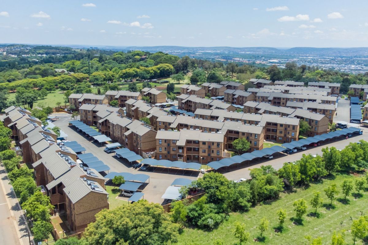 Aerial view of a residential apartment complex featuring multiple brick buildings, tiled roofs, and extensive covered parking areas within a landscaped estate.