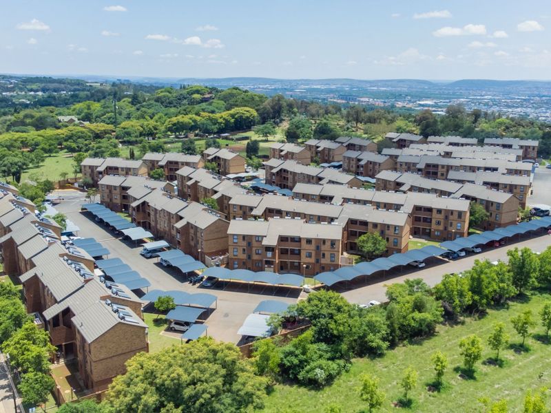 Aerial view of a residential apartment complex featuring multiple brick buildings, tiled roofs, and extensive covered parking areas within a landscaped estate.