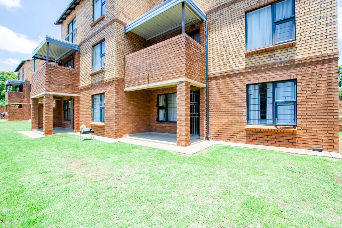 Rear view of a multi-story apartment building featuring face brick construction, covered ground-floor patios, and well-maintained lawn area.
