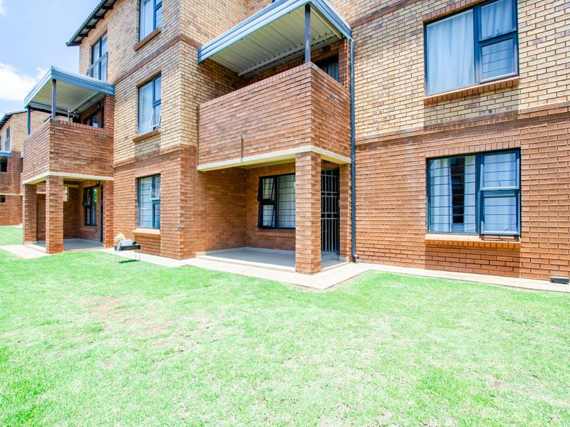 Rear view of a multi-story apartment building featuring face brick construction, covered ground-floor patios, and well-maintained lawn area.