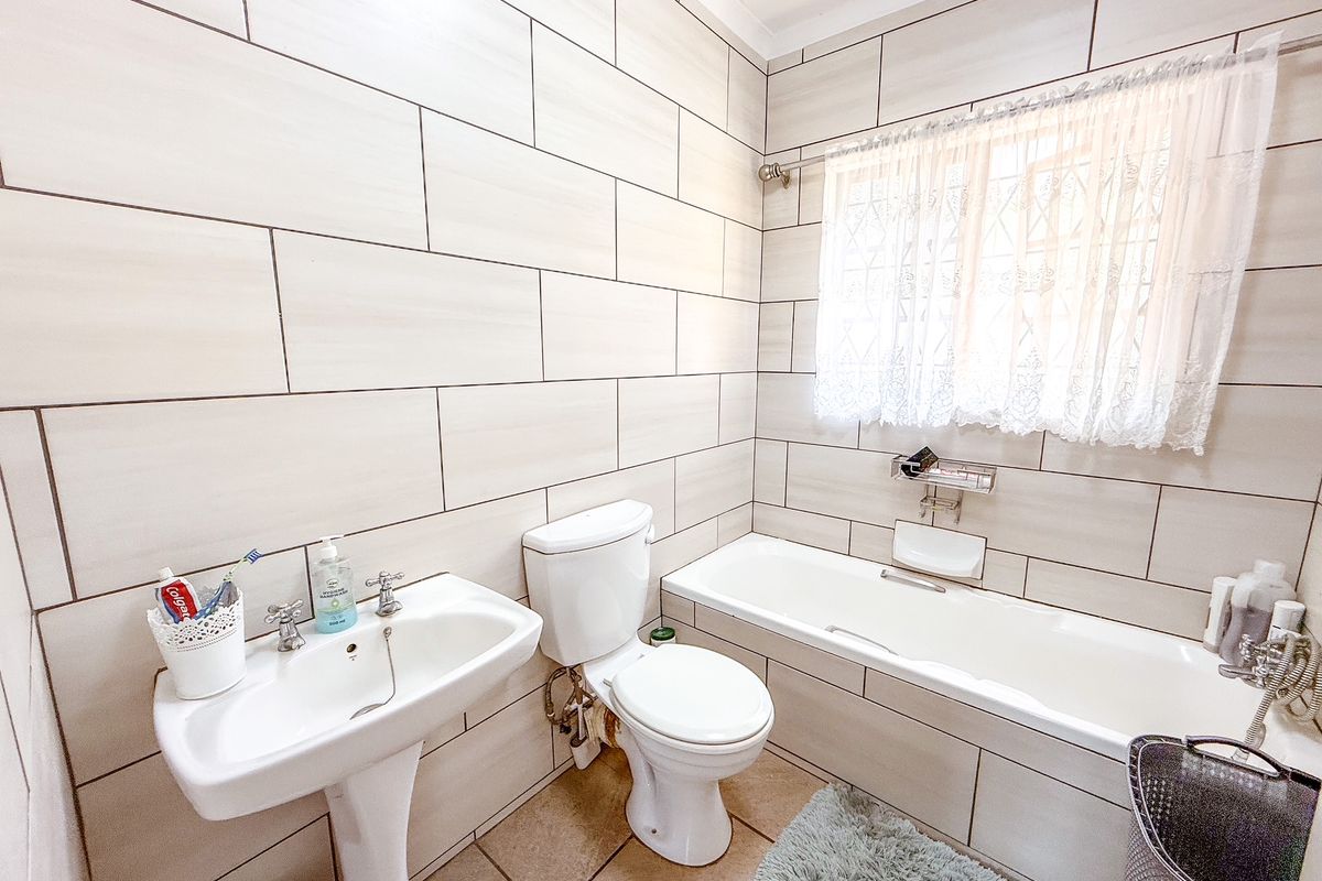 A clean, well-maintained bathroom featuring full-height wall tiling, a pedestal basin, a standard toilet, and a built-in bathtub with shower mixer.