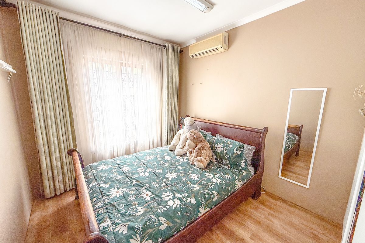 A bedroom featuring laminate flooring, a wall-mounted air conditioning unit, and a window with curtain tracks.