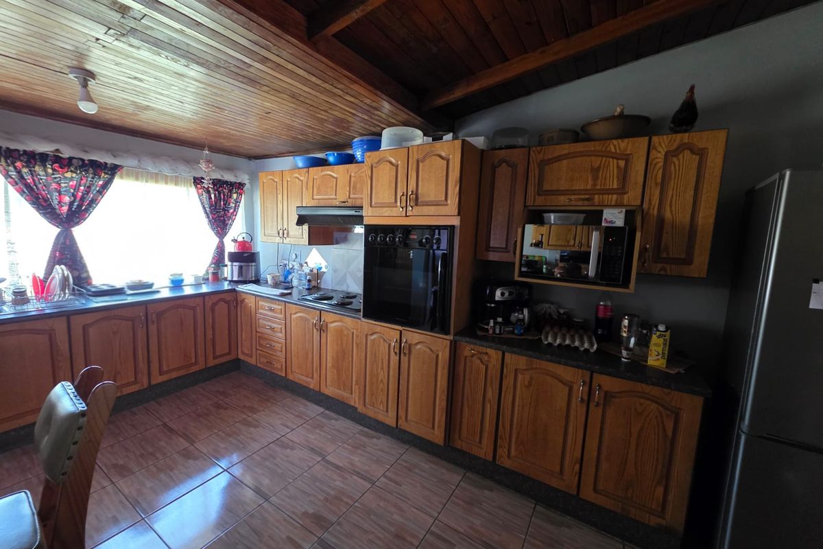A traditional kitchen featuring wood-toned cabinetry, tiled flooring, a built-in oven, and a timber-paneled ceiling.