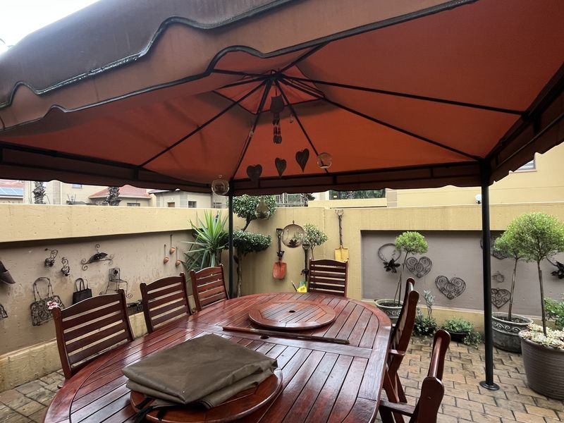 A covered outdoor patio area featuring a fixed gazebo structure, paved flooring, and enclosed by a solid boundary wall.