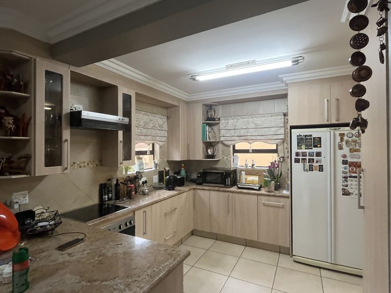 A functional kitchen featuring light wood cabinetry, granite countertops, an electric hob with extractor fan, and tiled flooring.