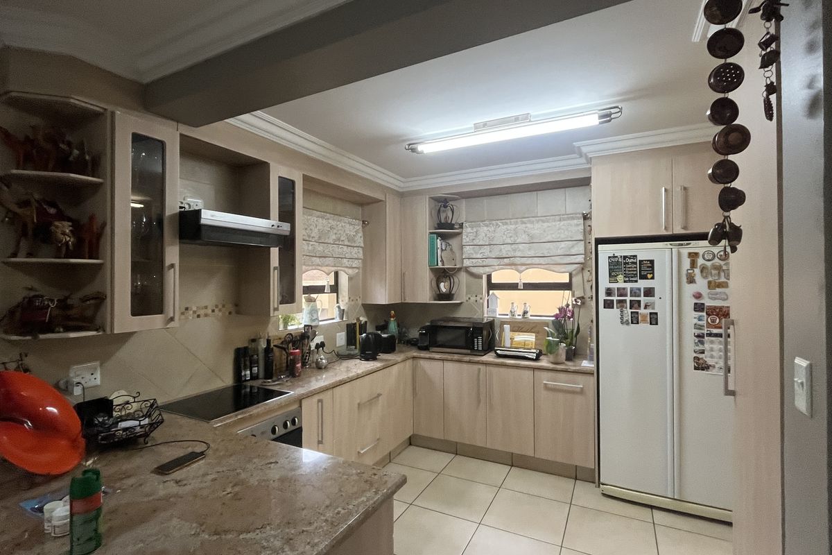A functional kitchen featuring light wood cabinetry, granite countertops, an electric hob with extractor fan, and tiled flooring.