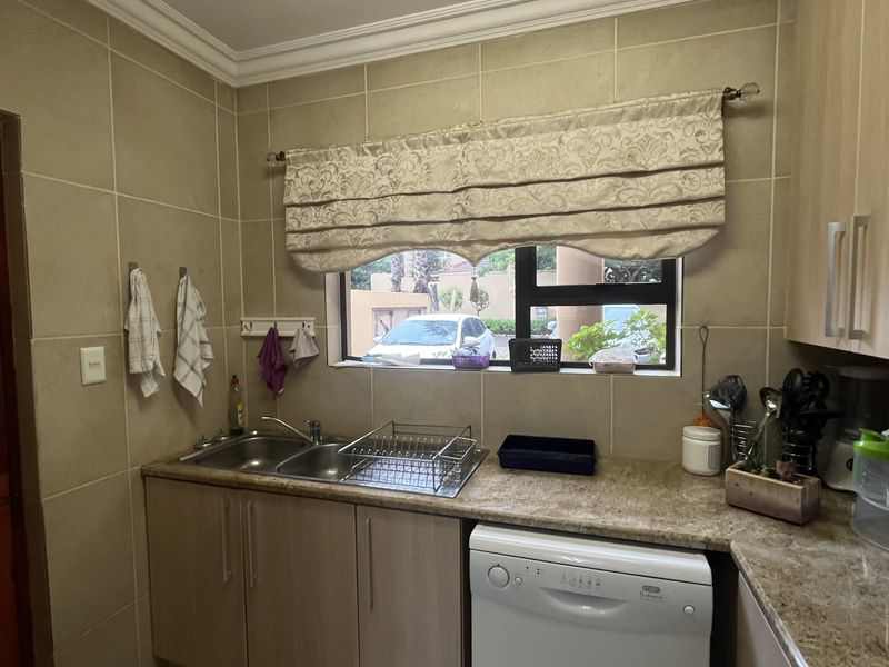A functional scullery area featuring granite countertops, a double basin sink, built-in cabinetry, and space for an integrated dishwasher.