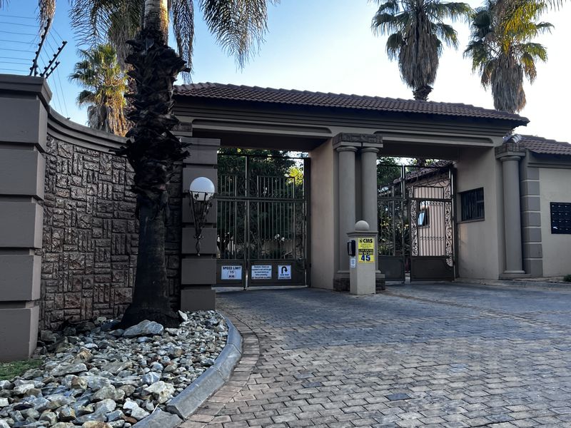 Secure gated entrance to the townhouse complex featuring stone-clad walls, electric fencing, and a paved driveway.