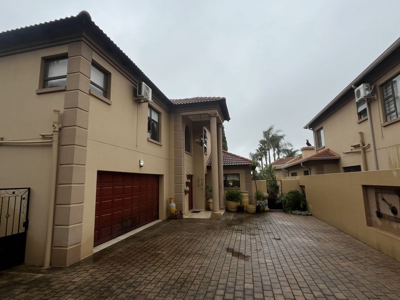 Front exterior view of a townhouse featuring a paved driveway, integrated garage, and covered entrance porch with decorative columns.