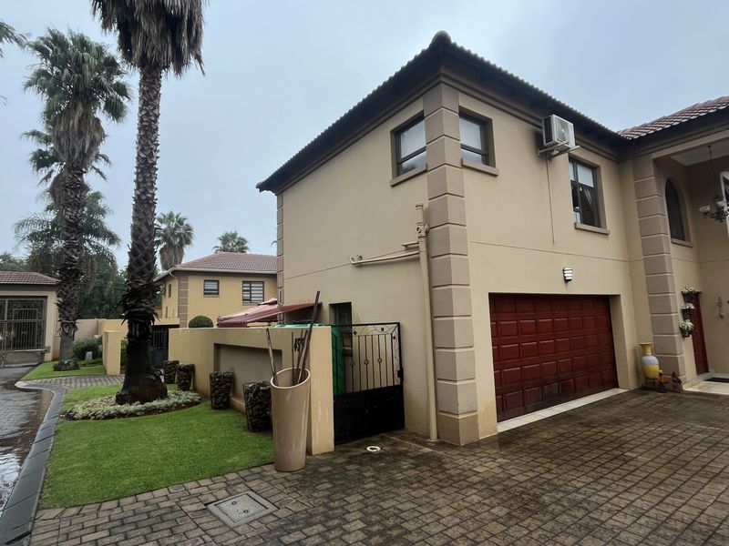 Front exterior view of a townhouse featuring a double garage, paved driveway, and a covered portico entrance with established garden landscaping.