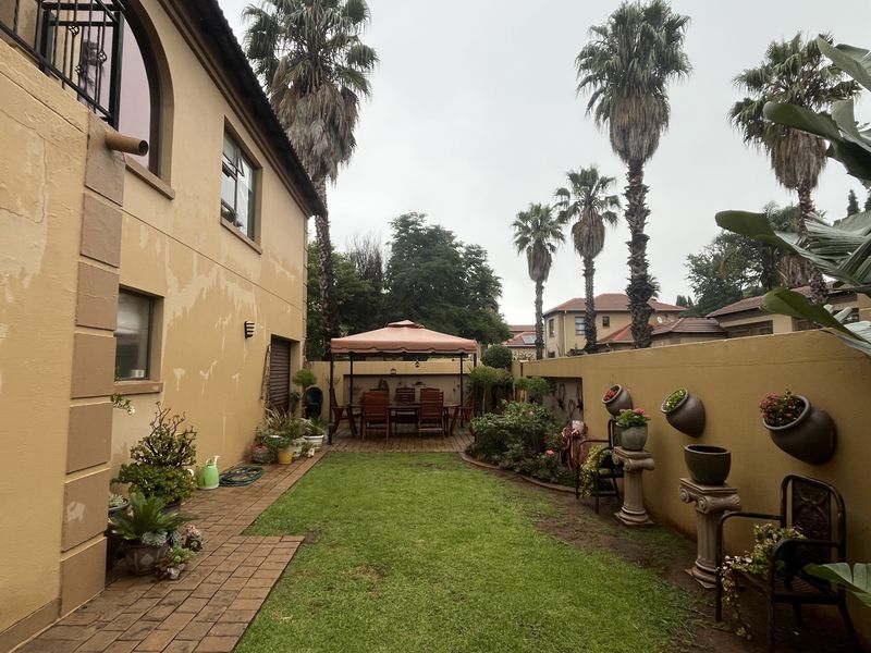 A rear garden area featuring a lawn, paved walkway, and boundary wall, with visible signs of wear on the exterior building facade.