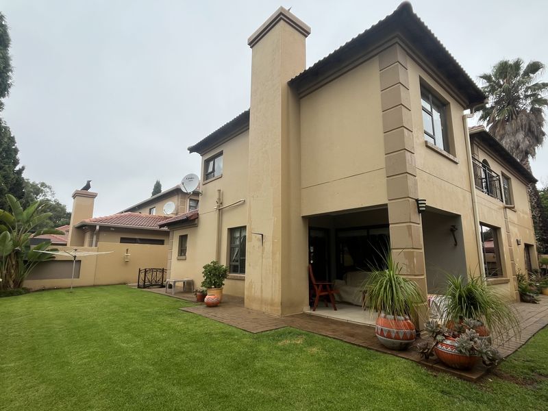Rear view of a two-story townhouse featuring a covered patio, paved outdoor area, and a well-maintained lawn with established garden landscaping.