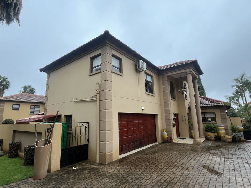 Front elevation of a double-story townhouse featuring a paved driveway, double garage, and classic architectural pillars.