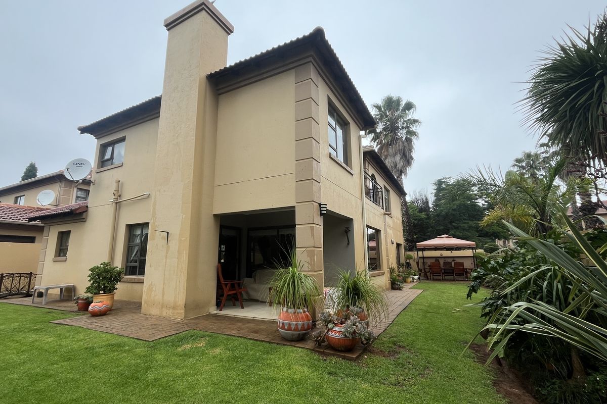Rear view of the townhouse featuring a paved patio area, chimney stack, and established garden lawn.