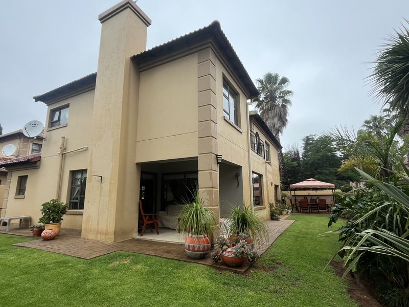 Rear view of the townhouse featuring a paved patio area, chimney stack, and established garden lawn.