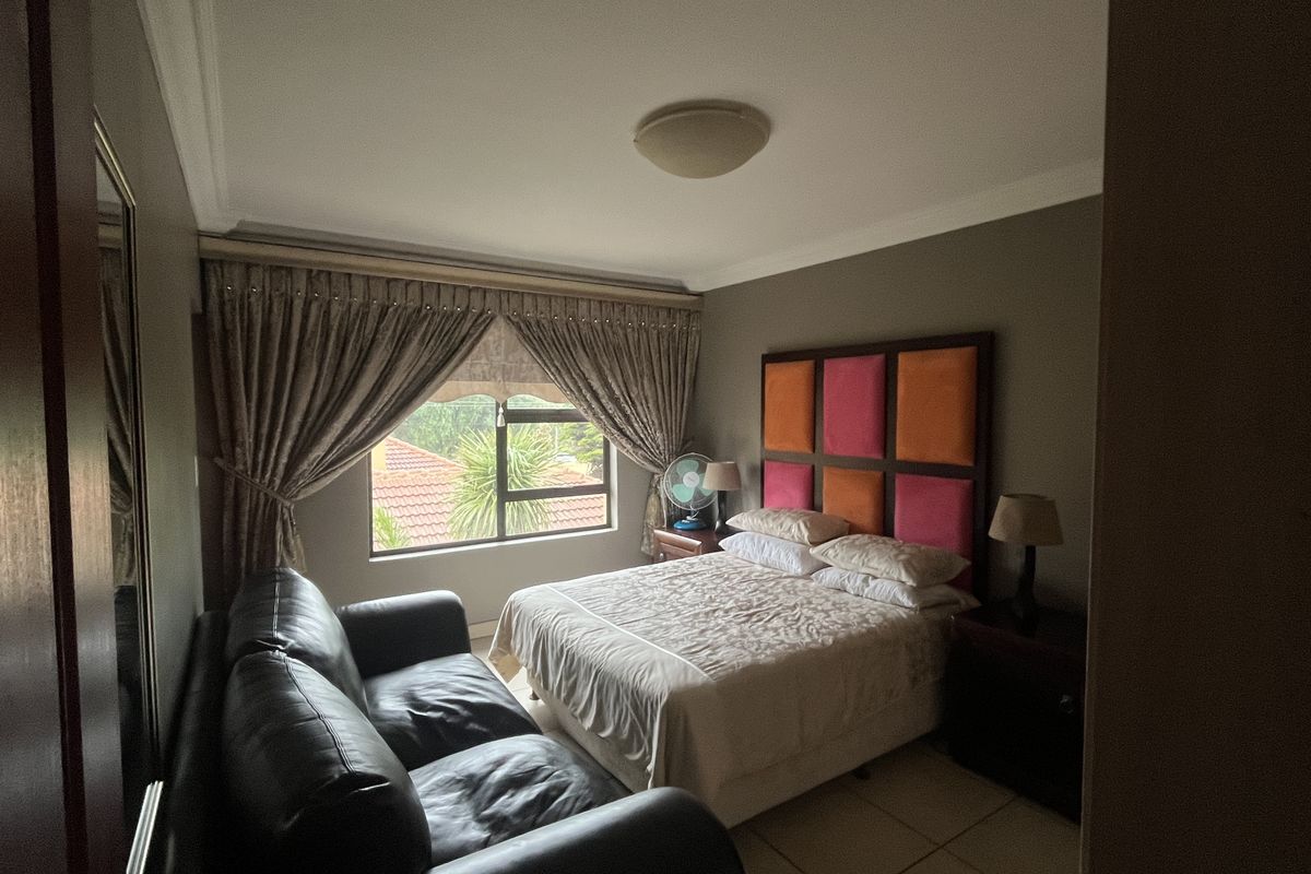 A bedroom featuring tiled flooring, cove cornicing, and an aluminium window frame, offering a functional space with neutral wall tones.