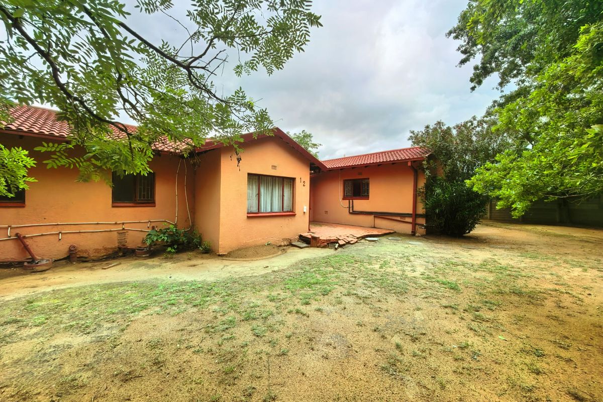 Rear view of a single-story house featuring a terracotta tiled roof, stucco exterior walls, and a small paved patio area in the backyard.