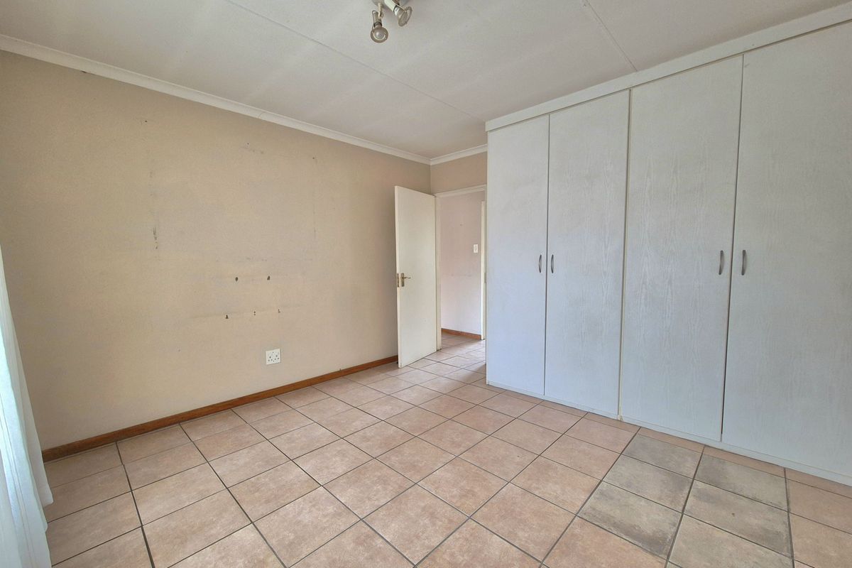 A spacious bedroom featuring built-in wardrobes, tiled flooring, and neutral wall finishes, offering a clean and functional living space.