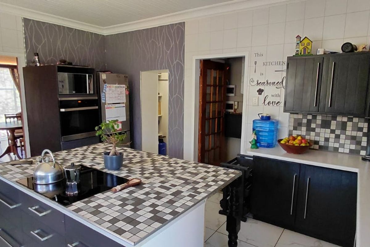 A functional kitchen featuring a central island with a built-in hob, dark cabinetry, tiled countertops, and an adjacent scullery area.