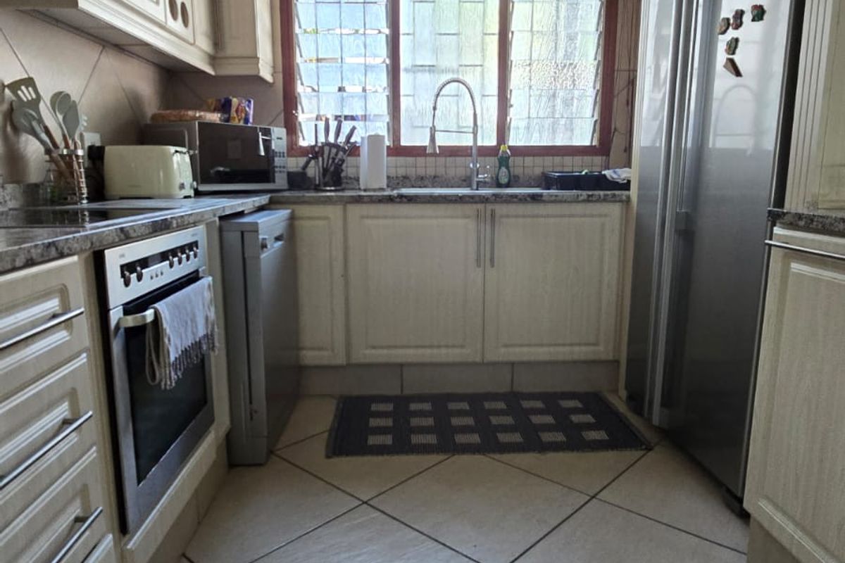 A functional galley-style kitchen featuring light-toned cabinetry, granite countertops, a built-in oven, and tiled flooring with a window above the sink.