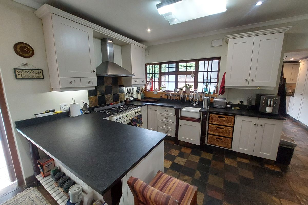 A well-appointed kitchen featuring white cabinetry, dark stone countertops, a farmhouse sink, a gas range with extractor hood, and slate tile flooring.