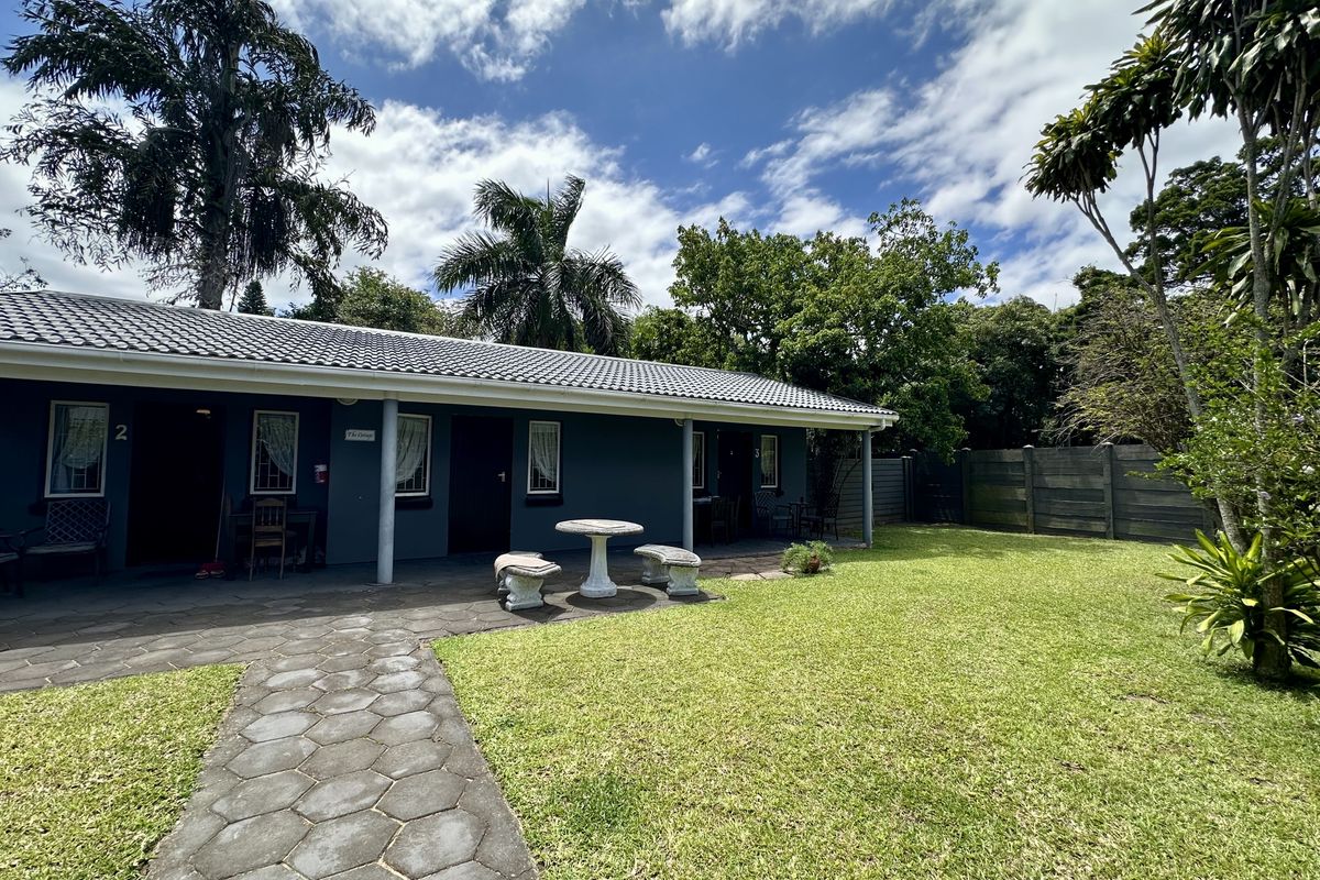 A well-maintained guest house exterior featuring a covered patio, paved walkway, and a spacious, landscaped garden area.