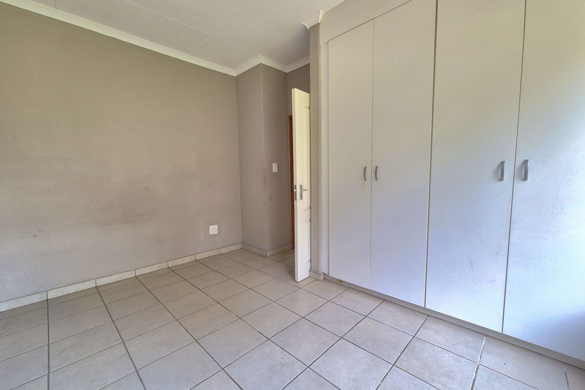 A vacant bedroom featuring neutral wall tones, tiled flooring, and built-in wardrobe storage.