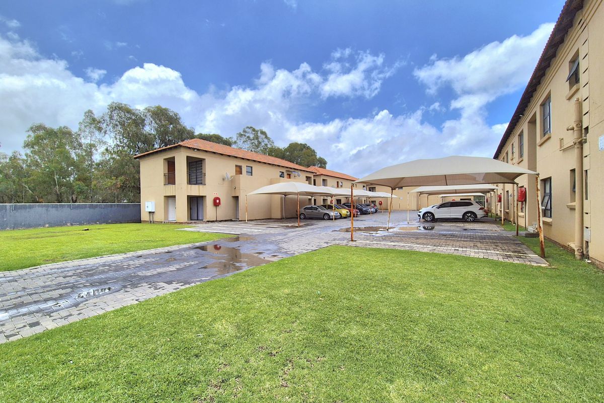 Exterior view of the apartment complex featuring paved parking bays with shade cloth carports and well-maintained communal lawn areas.