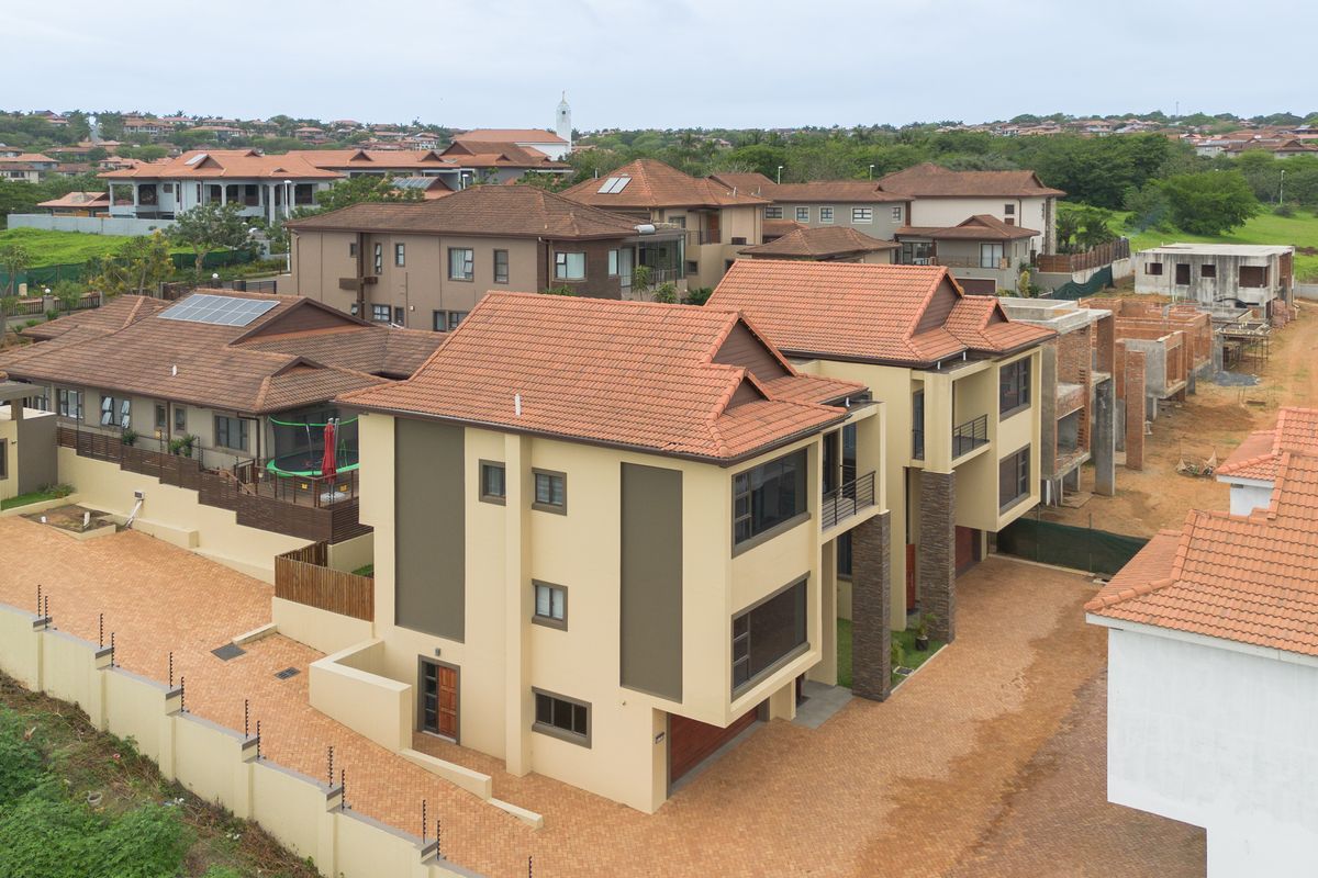 Aerial view of a modern townhouse complex featuring tiled roofs, paved driveways, and secure perimeter fencing within a residential estate.