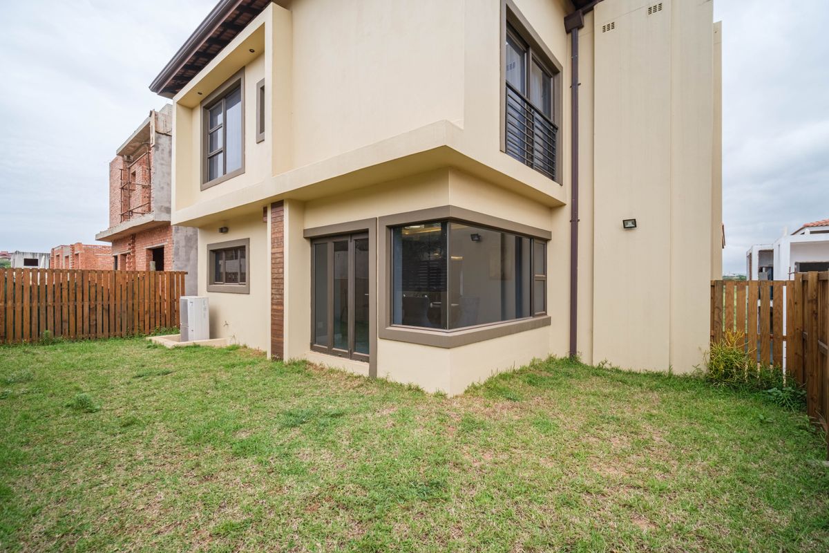 Rear view of a modern double-story townhouse featuring a private garden, corner windows, and aluminum-framed sliding doors.