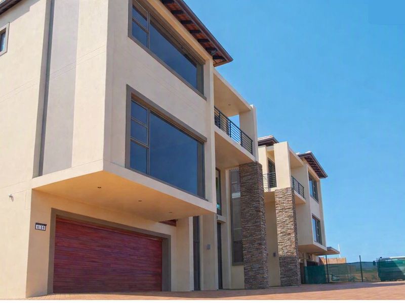 Modern multi-story residential facade featuring stone cladding, large aluminium windows, balconies, and a wooden double garage door.