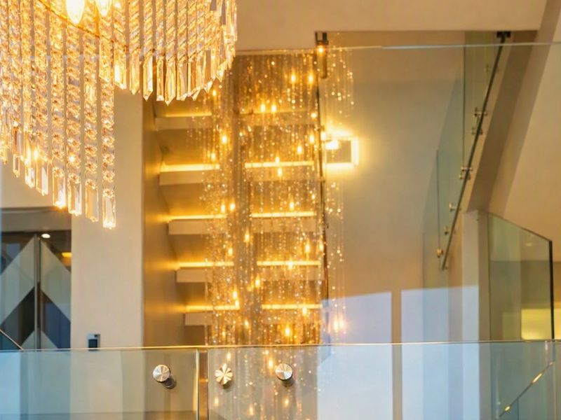 Elegant hallway featuring a modern glass balustrade, floating staircase with integrated lighting, and a prominent crystal chandelier.